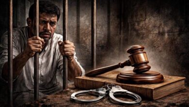 صورة مولدة بالذكاء الاصطناعي لرجل خلف القضبان، ممسكًا بالعتبات بإحكام، مع مطرقة العدالة وكتاب قانون وكلبشات أمامه، في زنزانة مظلمة ودرامية
